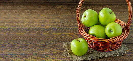 Organic Granny Smith apples in a wicker basket on wooden table. Banner