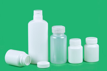 Five pills bottles on green background with copy space for text. Pharmaceutical product container. Pharmacy remedy pack.