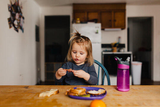 Cute toddler girl eating lunch and playing oranges at the kitchen table.