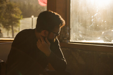 Portrait of a sad pensive reflective bearded man indoors with backlight on sunset