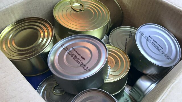 Tin cans with canned goods in a cardboard box - humane social assistance and food set to help those in need. Food collected for charity during coronavirus pandemic. Staple box - canned in metal jars.
