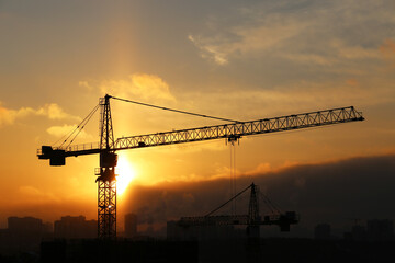 Silhouette of construction crane and unfinished residential building on sunrise background. Housing construction, apartment block in winter city