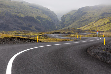An iconic icelandic road snakes through a mysty landscape and eventually into a canyon