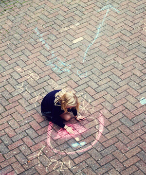 A little girl chalking on a pavement