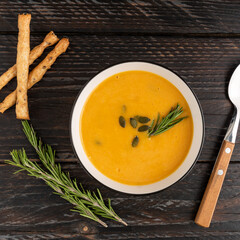 A bowl with pumpkin cream soup with grossini bread sticks and resemary on dark wooden background. Top view