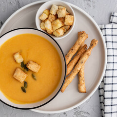 Top view of Pumpkin, carrot cream soup in a bowl. with croutons, pumpkin seeds and bread sticks.