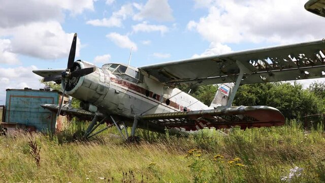 Broken and rusty old plane standing in thick grass of overgrown field against a cloudy blue sky
