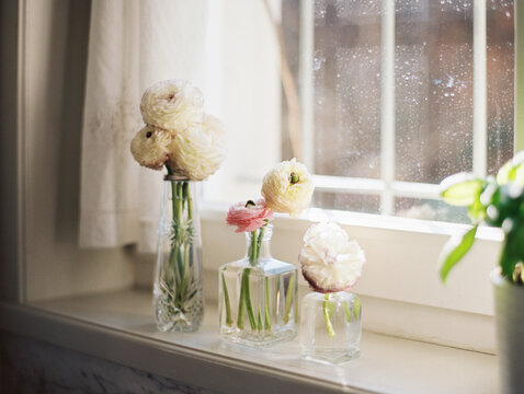 After the rain: colorful buttercups in glass vases on windowsill, window dirty with rain