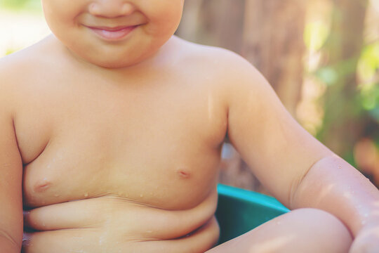 Crop image of fat boy sitting in the water in the basin. Little boy with fat and muscle