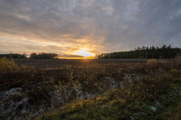 Sunset over a field with train-tracks and trees in the back next to a road