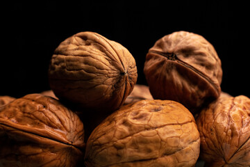 Walnuts in a pile, dramatically lit evenly from a slight angle, piled up against a pitch black background. The walnuts are fresh, tasty and full of nutritions.