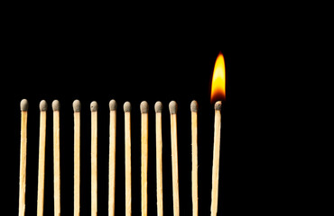 Burning match among unlit ones on dark background
