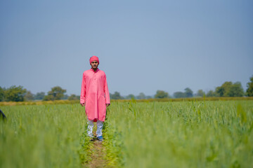 Young indian farmer standing his wheat field and giving happy expression