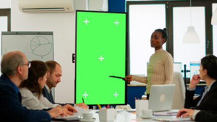 Diverse woman standing in start up office discussing strategy with green screen monitor in front of business partners. Manager explaining to multiethnic team project chroma key display mock up desktop