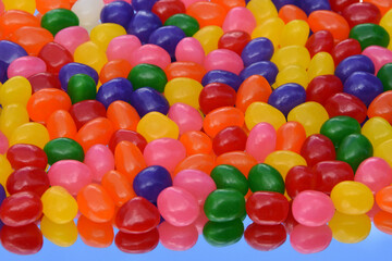 Colorful jellybeans on the mirror with its reflection against blue sky for background. Top view. 3-dimension.