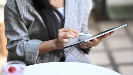 Cropped shot of young female freelancer working with digital tablet while sitting at cafe.