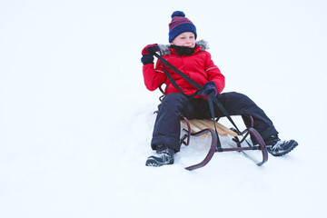 Fototapeta na wymiar Child sitting on a sled holding a cord in a winter. High quality photo