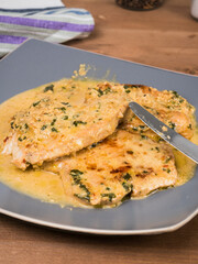 Fried turkey breast steaks with creamy sauce on a large plate with fork and knife on a wooden table