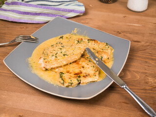 Fried turkey breast steaks with creamy sauce on a large plate with fork and knife on a wooden table