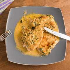 Fried turkey breast steaks with creamy sauce on a large plate with fork and knife on a wooden table