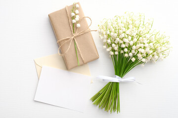 Bouquet of flowers lily of the valley, gift box and blank greeting card on white background. Happy Mother's Day or Woman's Day concept.