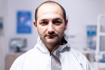 Close up of exhausted doctor in dental office looking on camera in the course of covid19 pandemic. Portrait of tired stomatologist wearing coronavirus ppe suit looking at camera.