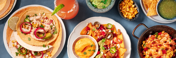 Mexican food, a panoramic banner on a blue background. Nachos, tacos, and other snacks and dips with cocktails