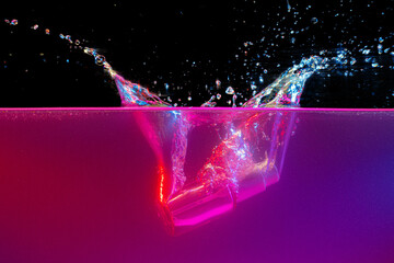 Glass bottle with dispenser diving into water against dark background