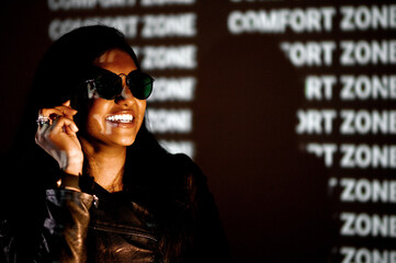 Young indian woman with sunglasses and black jacket posing at camera. Model smiling in dark studio...