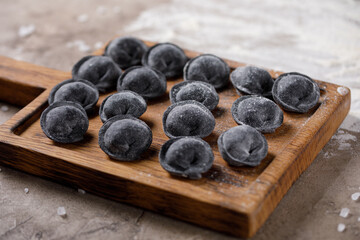 Traditional Russian dumplings, cuttlefish ink ravioli for dough, meat dumplings on a wooden board. View from above.
