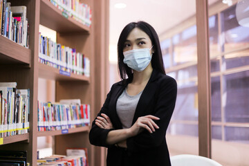 Beautiful Asian librarian woman  wear face masks  to prevent coronavirus, or COVID-19 new normal lifestyle in the library.