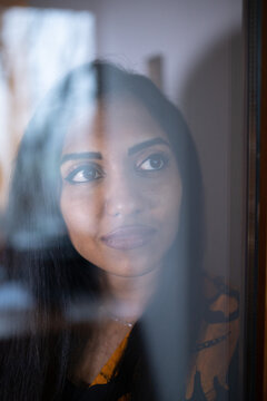 Portrait of a Indian smiling woman behind the window glass looking outside with serious face