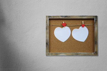Empty heart shape and wooden photo frame on gray wall.