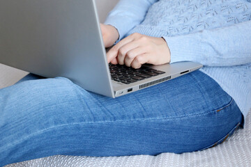 Woman in jeans sitting with laptop on a sofa, remote work at home. Concept of working on a computer at cozy atmosphere