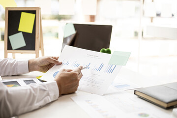 Fototapeta premium A businessman pointing at a document with a pen to check the financial numbers, he is sitting in his private office, the businessman examining the financial data from the corporate finance chart.