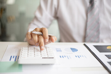 A businessman is using a white calculator to calculate financial numbers, he is sitting in his...