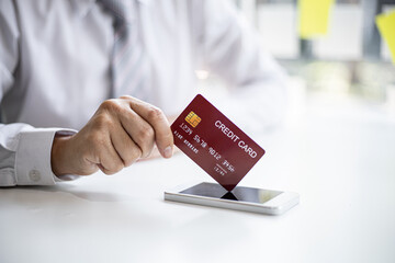 A businessman with a silver credit card, uses his credit card to pay for goods and services through a smartphone app, nowadays card payments are widely used around the world. Credit card concept.