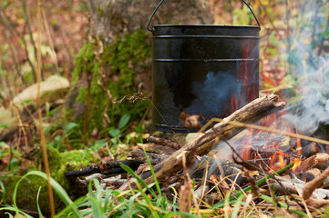 Hiking pot, Bowler in the bonfire. Fish soup boils in cauldron at the stake. Traveling, tourism, picnic cooking, cooking at the stake in a cauldron, fire and smoke.