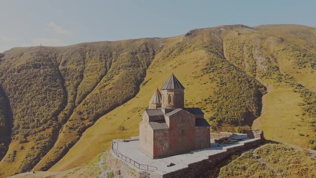 Slow motion aerial circle around Kazbegi trinity church on hill with background of caucasus mountains.Historical sites and georgian culture concept
