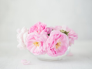 Bouquet of small light pink Roses in a glass vase against of pale grey wooden background. Selective focus. Shallow depth of field.