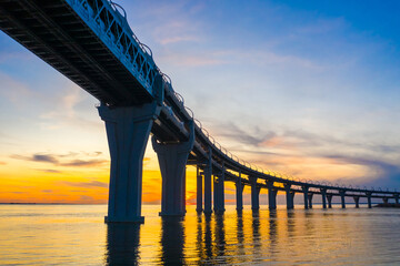 Road bridge on high supports above the water. Bridge against the sunset. Evening landscape. Roads. Travel by car. The highway passes over the bridge.