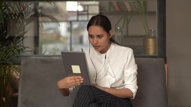 An angry businesswoman wearing earphones looking at tablet screen and warning with admonishing finger gesture, yelling at incompetent subordinate blaming for mistake in financial document.