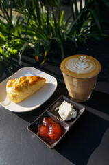 Close up hot cappuccino with heart shape latte art and Homemade Scone with Jam and Cream on dark  table at caff food and drink concept.