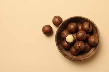 Bowl with tasty macadamia nuts on beige background
