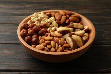 Bowl with different nuts on wooden background