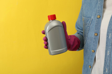 Woman in housework glove hold detergent on yellow background