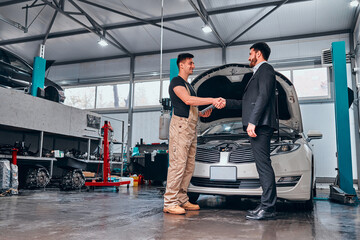 Smiling auto mechanic and client shaking hands in sevice.