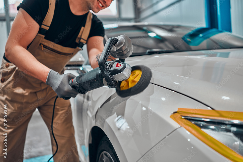 Wall mural Professional auto detailer hand holding rotary polisher while polishing paint surface of shiny white car.