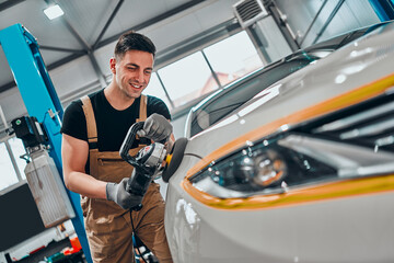 Auto mechanic worker polishing car at automobile repair and renew service station shop by power...
