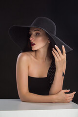 fashion portrait of a young and very beautiful girl in a black hat on a black background